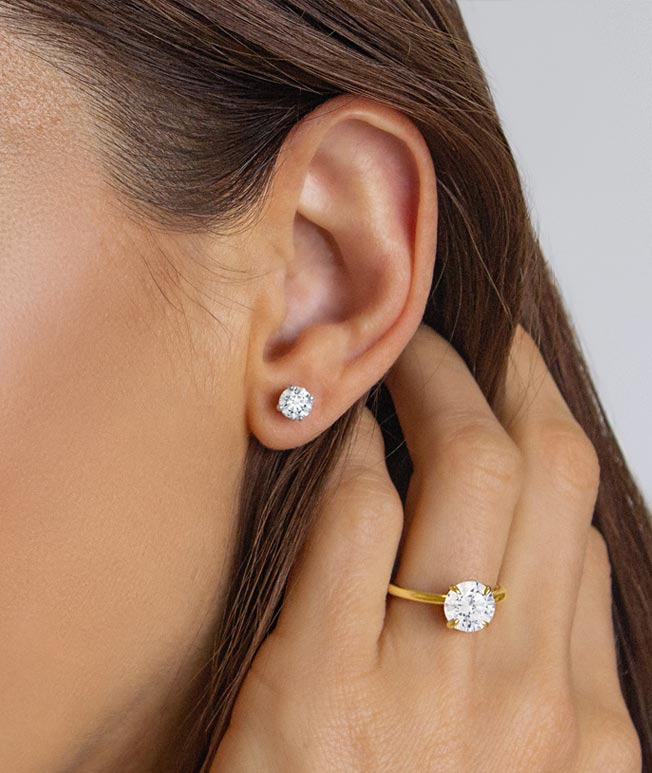 Woman wearing yellow gold diamond stud earrings and diamond ring.