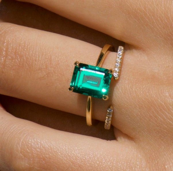 Model wearing gold emerald engagement ring and diamond wedding ring.