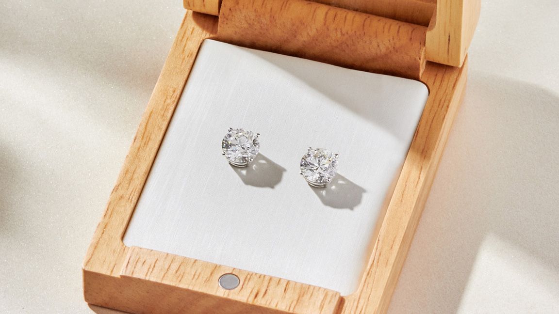 White gold diamond earrings inside a wooden jewelry box.