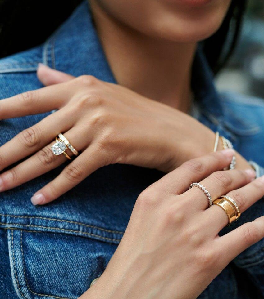 Model wearing gold diamond engagement ring, wedding ring, and assortment of fashion rings and bracelets.