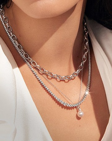 Model wearing assortment of layered chain, tennis, and pearl necklaces.